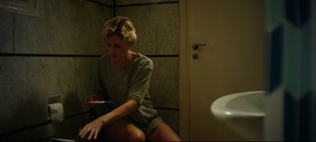 Movie still from “Monday” (2020), directed by Argyris Papadimitropoulos – A woman sitting on a toilet in a bathroom; Medium shot, High angle