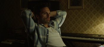 Movie still from “Monday” (2020), directed by Argyris Papadimitropoulos – A man sitting on a chair with his hands behind his head; Medium shot, High angle