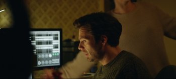 Movie still from “Monday” (2020), directed by Argyris Papadimitropoulos – A man looking at a computer screen while sitting in front of another man; Close Up shot, Over the shoulder angle