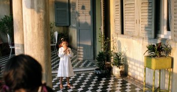 Movie still from “First They Killed My Father” (2017), directed by Angelina Jolie – A little girl standing in front of a building; Wide shot, High angle