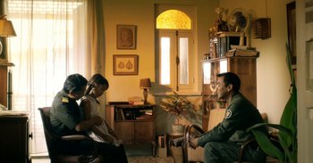 Movie still from “First They Killed My Father” (2017), directed by Angelina Jolie – A group of people sitting in a living room; Medium shot, High angle