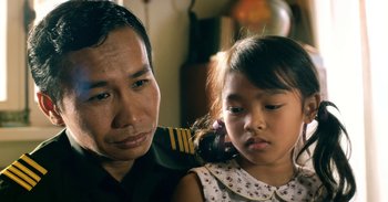 Movie still from “First They Killed My Father” (2017), directed by Angelina Jolie – A man and a little girl sitting next to each other; Close Up shot, Over the shoulder angle