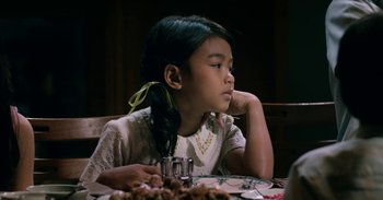 Movie still from “First They Killed My Father” (2017), directed by Angelina Jolie – A young girl sitting at a table with a plate of food in front of her; Close Up shot, Over the shoulder angle