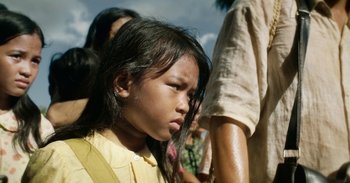 Movie still from “First They Killed My Father” (2017), directed by Angelina Jolie – A young girl is standing in a crowd of people; Close Up shot, Low angle