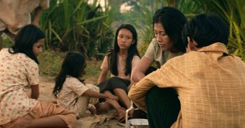 Movie still from “First They Killed My Father” (2017), directed by Angelina Jolie – A group of people sitting on the ground in the grass; Medium shot, High angle