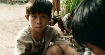 Movie still from “First They Killed My Father” (2017), directed by Angelina Jolie – A young boy sitting on the ground next to a group of people; Close Up shot, High angle
