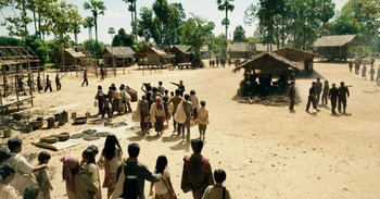 Movie still from “First They Killed My Father” (2017), directed by Angelina Jolie – A group of people standing on top of a dirt field; Extreme Wide shot, High angle