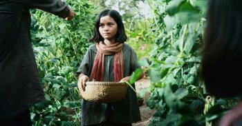 Movie still from “First They Killed My Father” (2017), directed by Angelina Jolie – A young girl holding a basket in her hands; Medium shot, Over the shoulder angle