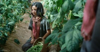 Movie still from “First They Killed My Father” (2017), directed by Angelina Jolie – A woman sitting on the ground holding a basket of green beans; Medium shot, High angle