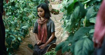 Movie still from “First They Killed My Father” (2017), directed by Angelina Jolie – A young girl sitting on the ground in the woods; Medium shot, High angle