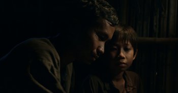 Movie still from “First They Killed My Father” (2017), directed by Angelina Jolie – A man and a boy sitting next to each other in the dark; Close Up shot, Over the shoulder angle