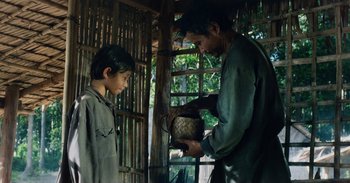 Movie still from “First They Killed My Father” (2017), directed by Angelina Jolie – A man and a boy are looking at a basket; Medium shot, Over the shoulder angle