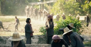 Movie still from “First They Killed My Father” (2017), directed by Angelina Jolie – A group of people standing on top of a dirt field; Wide shot, Over the shoulder angle