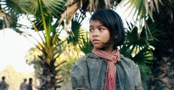 Movie still from “First They Killed My Father” (2017), directed by Angelina Jolie – A young girl wearing a plaid scarf and a jacket; Close Up shot, Low angle