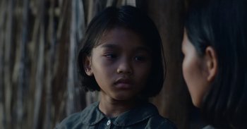 Movie still from “First They Killed My Father” (2017), directed by Angelina Jolie – A young asian girl with dark hair and blue eyes looking at the camera; Close Up shot, Over the shoulder angle