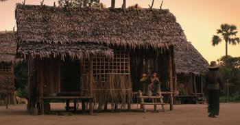 Movie still from “First They Killed My Father” (2017), directed by Angelina Jolie – A person sitting in front of a hut on a dirt ground; Extreme Wide shot, Low angle