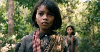 Movie still from “First They Killed My Father” (2017), directed by Angelina Jolie – A young girl wearing a scarf standing next to another young girl; Close Up shot, Over the shoulder angle