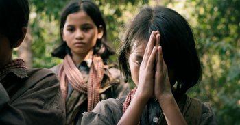 Movie still from “First They Killed My Father” (2017), directed by Angelina Jolie – Two young girls are praying in a forest; Close Up shot, Low angle