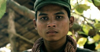 Movie still from “First They Killed My Father” (2017), directed by Angelina Jolie – A man wearing a green hat and a plaid shirt; Close Up shot, Over the shoulder angle