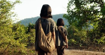 Movie still from “First They Killed My Father” (2017), directed by Angelina Jolie – Two people walking on a dirt path near a forest; Medium shot, Low angle