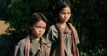 Movie still from “First They Killed My Father” (2017), directed by Angelina Jolie – Two young girls standing next to each other in front of a bush; Close Up shot, Low angle