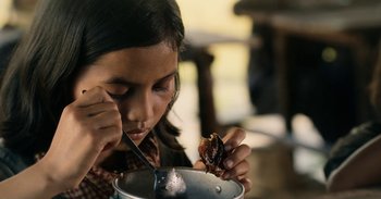 Movie still from “First They Killed My Father” (2017), directed by Angelina Jolie – A young girl is eating food from a bowl; Extreme Close Up shot, High angle