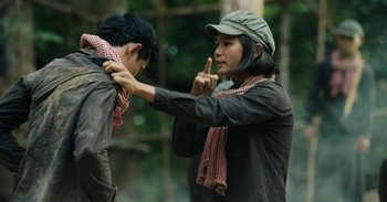 Movie still from “First They Killed My Father” (2017), directed by Angelina Jolie – A person with a hat and a scarf on; Medium shot, Over the shoulder angle