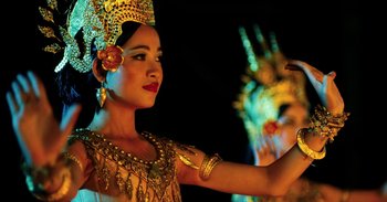 Movie still from “First They Killed My Father” (2017), directed by Angelina Jolie – A woman in a gold dress and a crown is dancing; Close Up shot, Low angle