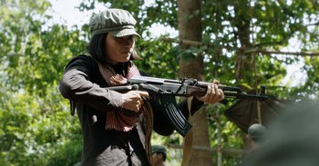 Movie still from “First They Killed My Father” (2017), directed by Angelina Jolie – A woman is holding a rifle in her hands; Medium shot, Over the shoulder angle
