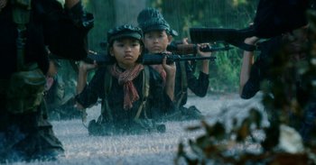 Movie still from “First They Killed My Father” (2017), directed by Angelina Jolie – Two young children are sitting in the rain while holding guns; Medium shot, Low angle