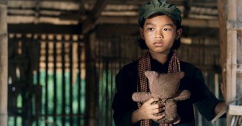 Movie still from “First They Killed My Father” (2017), directed by Angelina Jolie – A young boy holding a teddy bear in his hands; Close Up shot, Over the shoulder angle