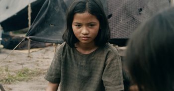 Movie still from “First They Killed My Father” (2017), directed by Angelina Jolie – A young girl is standing outside in the dirt; Close Up shot, Over the shoulder angle