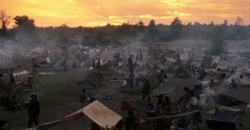 Movie still from “First They Killed My Father” (2017), directed by Angelina Jolie – A group of people standing around tents in a field; Extreme Wide shot, High angle