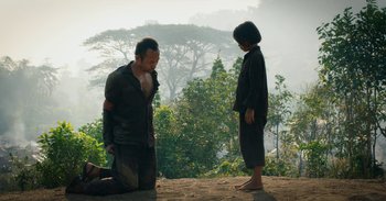 Movie still from “First They Killed My Father” (2017), directed by Angelina Jolie – A man kneeling down next to a woman on the ground; Wide shot, Over the shoulder angle