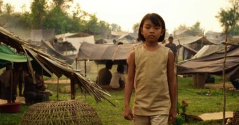 Movie still from “First They Killed My Father” (2017), directed by Angelina Jolie – A young girl standing in front of a group of tents; Medium shot, Over the shoulder angle