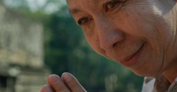 Movie still from “First They Killed My Father” (2017), directed by Angelina Jolie – An older woman is praying with her hands in front of her face; Extreme Close Up shot, Low angle