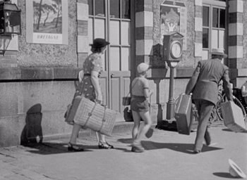 Movie still from “Monsieur Hulot's Holiday” (1953), directed by Jacques Tati – An old photo of people walking down the street carrying luggage; Wide shot, Low angle