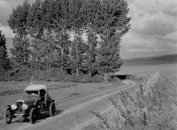 Movie still from “Monsieur Hulot's Holiday” (1953), directed by Jacques Tati – An old car driving down a dirt road near a forest; Extreme Wide shot, High angle