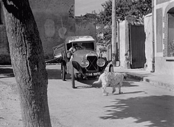 Movie still from “Monsieur Hulot's Holiday” (1953), directed by Jacques Tati – An old photo of a dog and a car on the side of the road; Wide shot, High angle