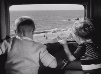 Movie still from “Monsieur Hulot's Holiday” (1953), directed by Jacques Tati – Two young boys sitting in the back of a car looking out a window at the beach; Wide shot, High angle