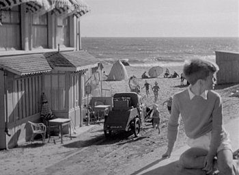 Movie still from “Monsieur Hulot's Holiday” (1953), directed by Jacques Tati – An old black and white photo of people on the beach and an old car; Wide shot, High angle