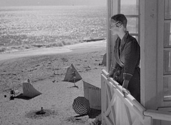 Movie still from “Monsieur Hulot's Holiday” (1953), directed by Jacques Tati – A woman standing on a balcony looking out at the beach; Wide shot, High angle