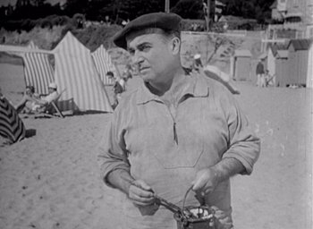 Movie still from “Monsieur Hulot's Holiday” (1953), directed by Jacques Tati – An old photo of a man eating food on the beach; Medium shot, Low angle