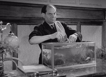 Movie still from “Monsieur Hulot's Holiday” (1953), directed by Jacques Tati – An old black and white photo of a man holding a fish tank; Medium shot, Low angle