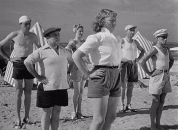 Movie still from “Monsieur Hulot's Holiday” (1953), directed by Jacques Tati – A group of people standing on top of a sandy beach; Medium shot, Low angle