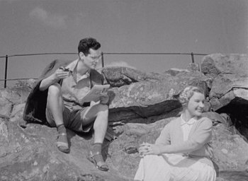 Movie still from “Monsieur Hulot's Holiday” (1953), directed by Jacques Tati – A man and a woman sitting on a rocky cliff; Medium shot, High angle