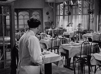 Movie still from “Monsieur Hulot's Holiday” (1953), directed by Jacques Tati – An old photo of people sitting at tables in a restaurant; Wide shot, High angle