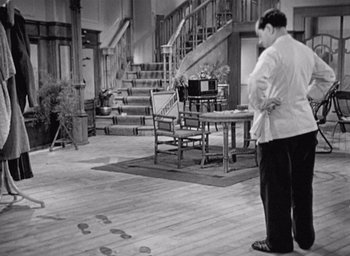 Movie still from “Monsieur Hulot's Holiday” (1953), directed by Jacques Tati – A black and white photo of a man standing in front of a table; Wide shot, High angle