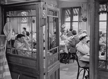 Movie still from “Monsieur Hulot's Holiday” (1953), directed by Jacques Tati – A group of people sitting at tables in a restaurant; Wide shot, High angle