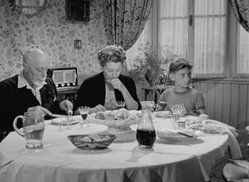 Movie still from “Monsieur Hulot's Holiday” (1953), directed by Jacques Tati – An old photo of people sitting at a dinner table; Medium shot, High angle